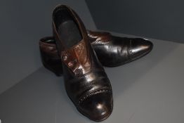 A pair of antique black and brown leather boots having buttons to sides and stack heel, around a