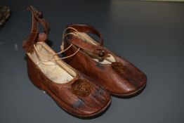 A pair of brown leather baby shoes having pom-pom's to the fronts and strap with button fastening.