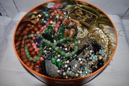 A tin containing a selection of costume jewellery including earrings, spoon bangle, beads etc