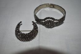 A cut steel tension bangle having pierced lozenge shaped panel and concealed clasp and a similar cut