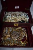 A maroon coloured jewellery box containing a selection of costume jewellery chains and beads