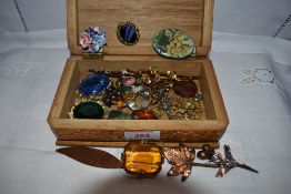 A small wooden box containing a selection of costume brooches and scarf clips including enamelled,
