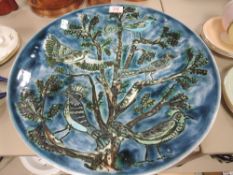 A large studio pottery charger by Poole having deep blue green hues with imagery of birds in tree