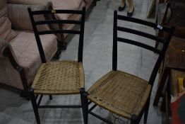 A pair of ebonised rail back dining chairs having strung seats