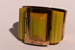 An Art Deco brass and amber style celluloid bangle having a hinged powder compartment to top and a