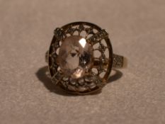 A lady's dress ring having a morganite style oval stone within an open border having diamond chip
