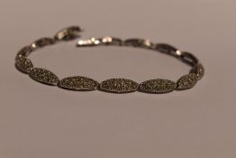 A 9ct white gold articulated bracelet having 14 gem set lozenge shaped panels and a concealed box