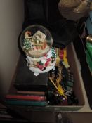 A box of toy cars, dominoes and a snow globe having christmas scene.