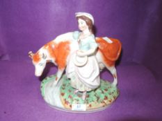 A Staffordshire style figurine depicting milk maid and cow.