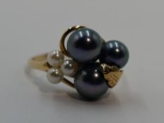 A lady's dress ring having black and white cultured pearls in a yellow metal stylised mount on a