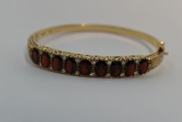 A 9ct gold hinged bangle set with nine oval garnets interspersed by pairs of diamond chips in a