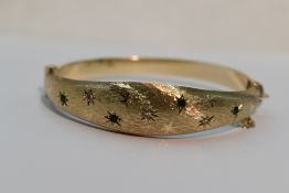A 9ct gold hinged bangle having diamond and emerald chip decoration in star burst settings on
