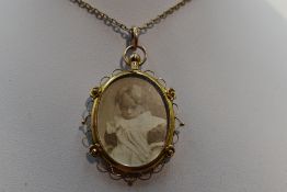 A glass locket of oval form having a decorative 9ct gold mount on a yellow metal chain stamped 9ct
