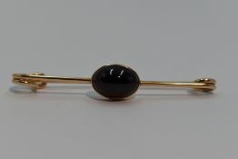 A yellow metal bar brooch in the form of a safety pin having a garnet cabouchon, no marks tests as