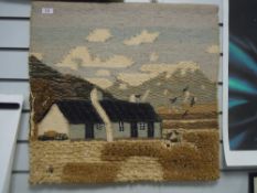 A wool wall hanging depicting a croft with lobster pots and hills.