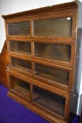 An early 20th Century plain oak wide four tier stacking bookcase having stepped base, pane of