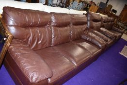 A modern brown leatherette or bycast leather lounge suite comprising two three seater settees and