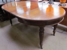 An Edwardian oak extending dining table with two additional leaves on reeded and fluted legs and