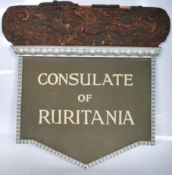 A 20th century shaped wooden sign for the ' Consulate Of Ruritania '. The sign having applied wooden