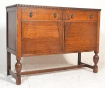 A 1930's oak sideboard being raised on cup and cover legs having twin cupboard doors under short