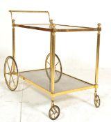 A mid century italian brass and smoked glass trolley table raised on original castors having twin