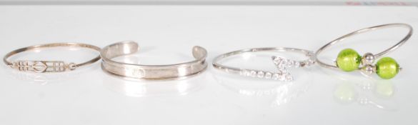 A group of silver bangles to include an open bangle with green glass beads, a hook and eye bangle