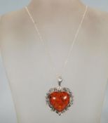 A large silver and amber style heart shaped pendant necklace having a decorative floral silver mount