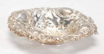 A silver pin dish of round form having rococo repousse and pierced decoration having a flared rim.