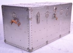 A large vintage metal covered travel trunk having brown leather carrying handles with blue lined