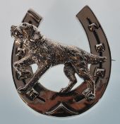 A large sterling silver brooch in the form of a horse shoe. An engraved dog is placed over the