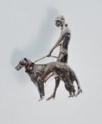 A figural sterling silver brooch depicting a figure walking a dog on a lead. The dogs collar is