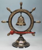 A 20th Century brass dinner bell having a ships wheel raised on a round stepped pedestal base with a