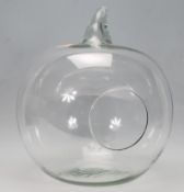 A contemporary glass terrarium in the form of a pumpkin having a round opening to the back with a
