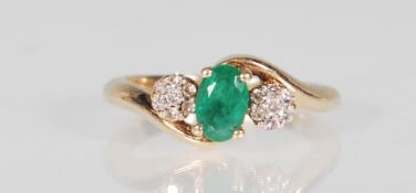 An 9ct yellow gold ladies dress ring set with a central faceted cut oval emerald flanked by clusters