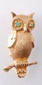 A gold and emerald figural brooch pin. The brooch in the form of an owl perched upon a branch
