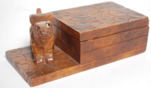 An early 20th Century Folk Art carved wooden cigarette box of rectangular form raised on a plinth