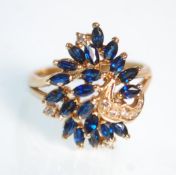 A decorative 14ct yellow gold ladies ring set with sapphires and diamond chips to a peacock style