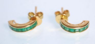 A pair of 18k yellow gold half hoop earrings set with faceted square cut emeralds. Stamped 18k.
