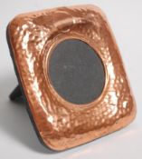 An arts and crafts style copper picture frame of square form having hammered decoration with a round