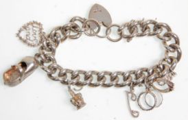 A thick link silver chain charm bracelet adorned with charms to include three textuard rings, crown,