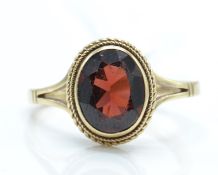 A hallmarked 9ct gold and garnet ring. The ring having an oval mixed cut garnet surrounded by a rope