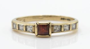 A 9ct gold ruby and diamond ring. The ring with cushion cut ruby flanked by inset diamonds to the