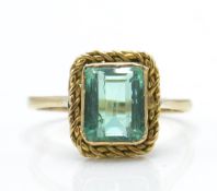 A 9ct gold and emerald ring. The ring set with a facet cut emerald in mount with rope twist border