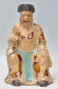 A late 19th / early 20th Century Chinese earthenware figurine in the form of a seated monk wearing a