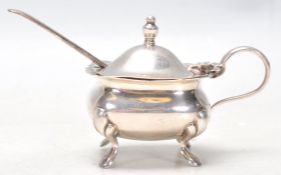 A hallmarked Sterling silver mustard pot set upon four figured feet with a hinged lid and finial