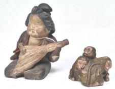 An Antique Japanese clay figure in the form of a seated gashsia playing a musical instrument with