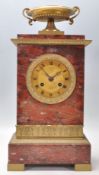 An early 20th Century red marble mantel clock of upright rectangular form having a brass urn atop