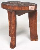An Australian aboriginal wooden tribal stool having a around seat with three carved legs below,