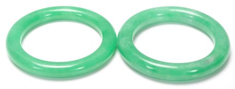 A pair of 20th Century Chinese green stone jade style slave bangles of round plain form.