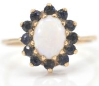 A 9ct gold hallmarked opal and sapphire cluster ring. The central oval cabochon within a halo of